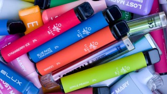 A pile of colorful disposable vape pens with various flavors labeled, such as strawberry ice, blue razz lemonade, mango, apple peach and blueberry raspberry.