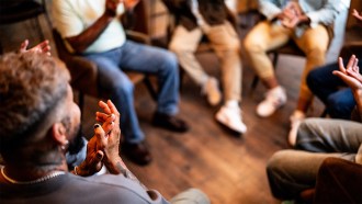 A photo showing people's legs as they sit in chairs set up in a circle.