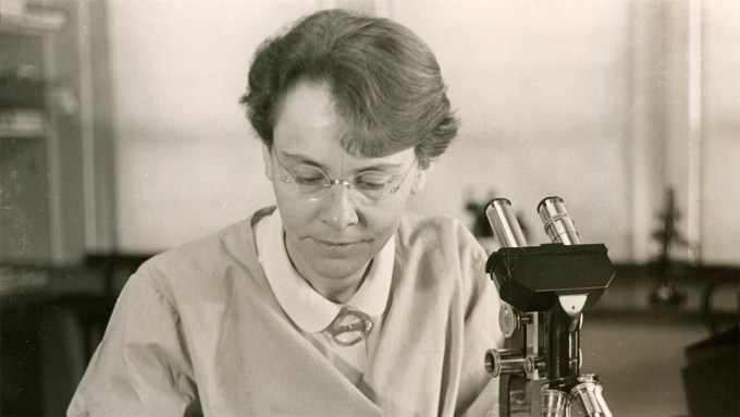 Barbara McClintock, an American biologist who won the 1983 Nobel Prize in physiology or medicine looking down with a microscope next to her face