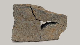 A gray rock with rust-colored specks. The rock is broken into three pieces but put back together like a puzzle. The middle is missing because that was taken to test a new rock analysis tool.