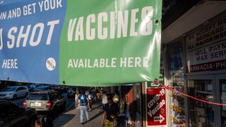 A blue and green banner and a red sign advertise the availability of COVID-19 vaccines outside a pharmacy in Brooklyn.