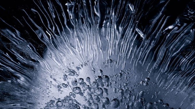 an image of ice shows bubbles and striations radiating from lower center. Regular ice like this can only generate a weak current, but when slabs of saltwater ice are bent, they can produce a stronger electrical current, known as the flexoelectric effect.
